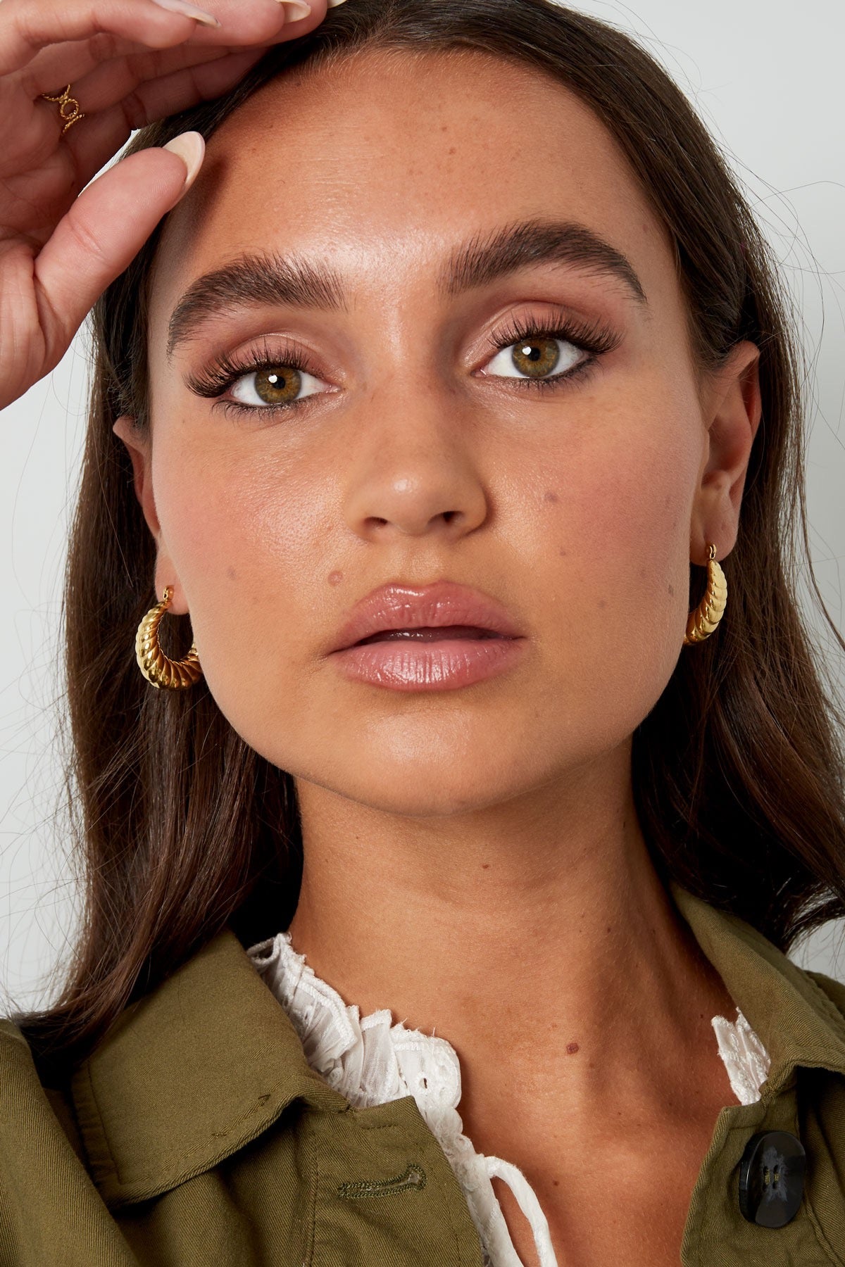 Oorbellen | Aesthetic van Louxx the brand, een model met een hand op haar hoofd en goudkleurige hoepel oorbellen.