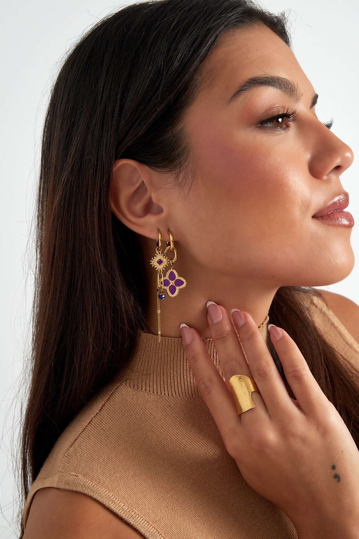Model poseert met gouden oorbellen met paarse bloemvormige hanger, onderdeel van de 'Oorbellen | Flower' lijn van Louxx the brand.