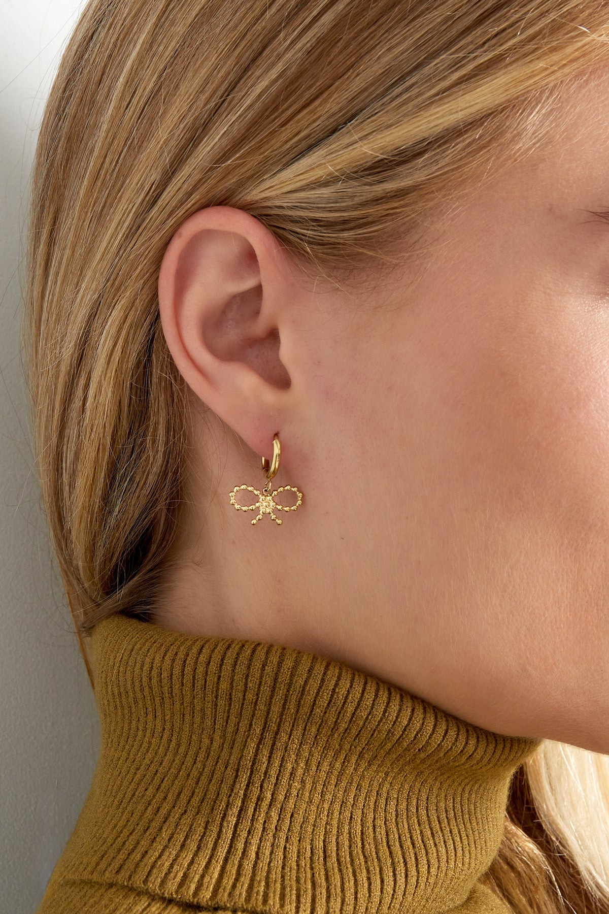 Model draagt de Oorbellen | Strikje van Louxx the brand, met een gouden strikjesontwerp. Ideaal voor elke gelegenheid.