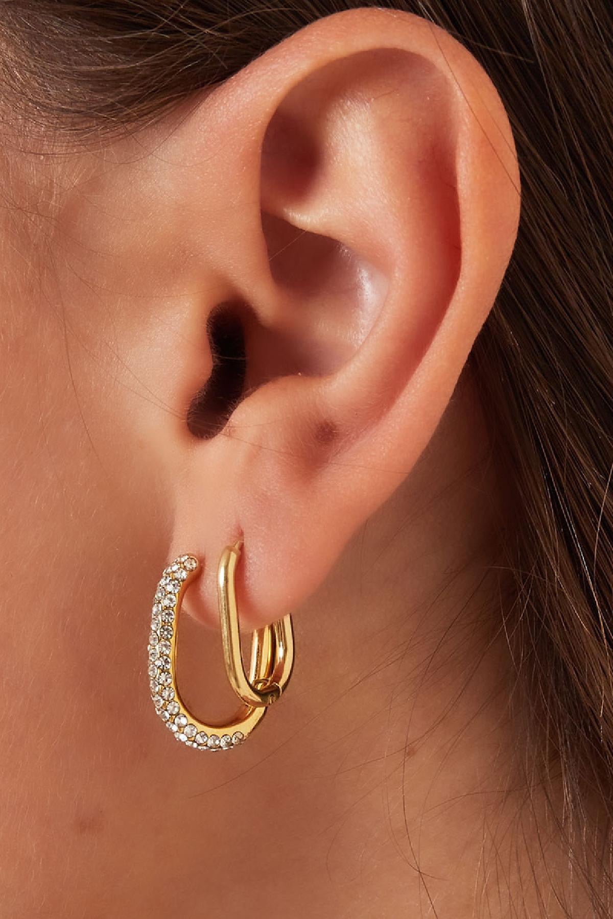 Oorbellen | Ovale Hoepels van Louxx the brand, gedragen met een elegant oor, waarbij de glinsterende steentjes accentueren de gouden hoepels.