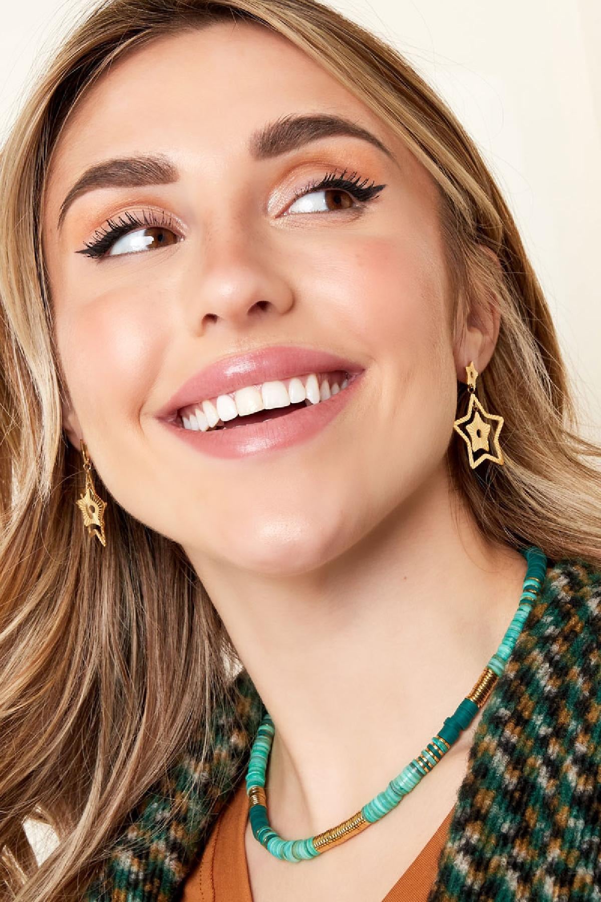 Een persoon die de Oorbellen | Sterren van Louxx the brand draagt, lachend en zichtbaar genietend van haar stijlvolle look met een kleurrijke ketting.