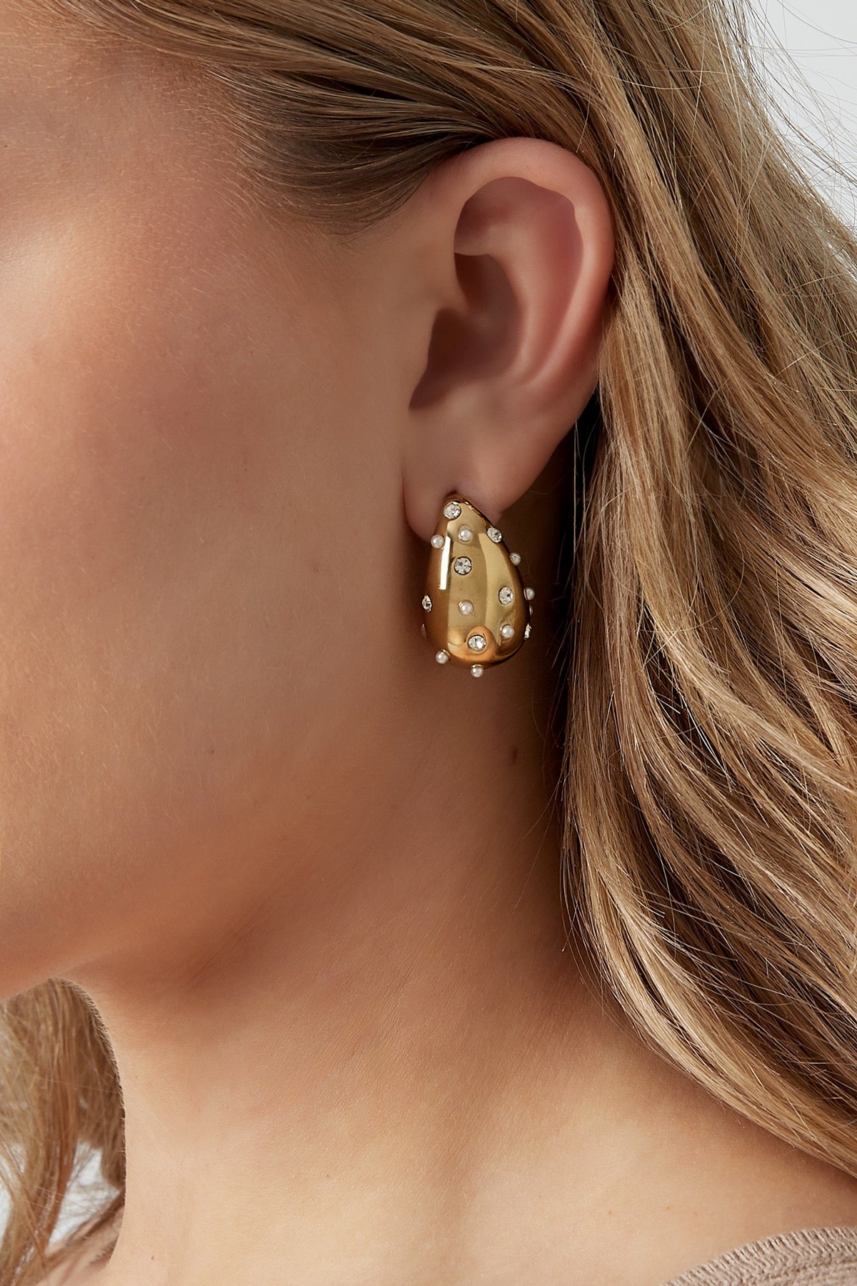 Een model draagt de gouden druppel oorbellen van Louxx the brand, die prachtig glanzen met kristallen.