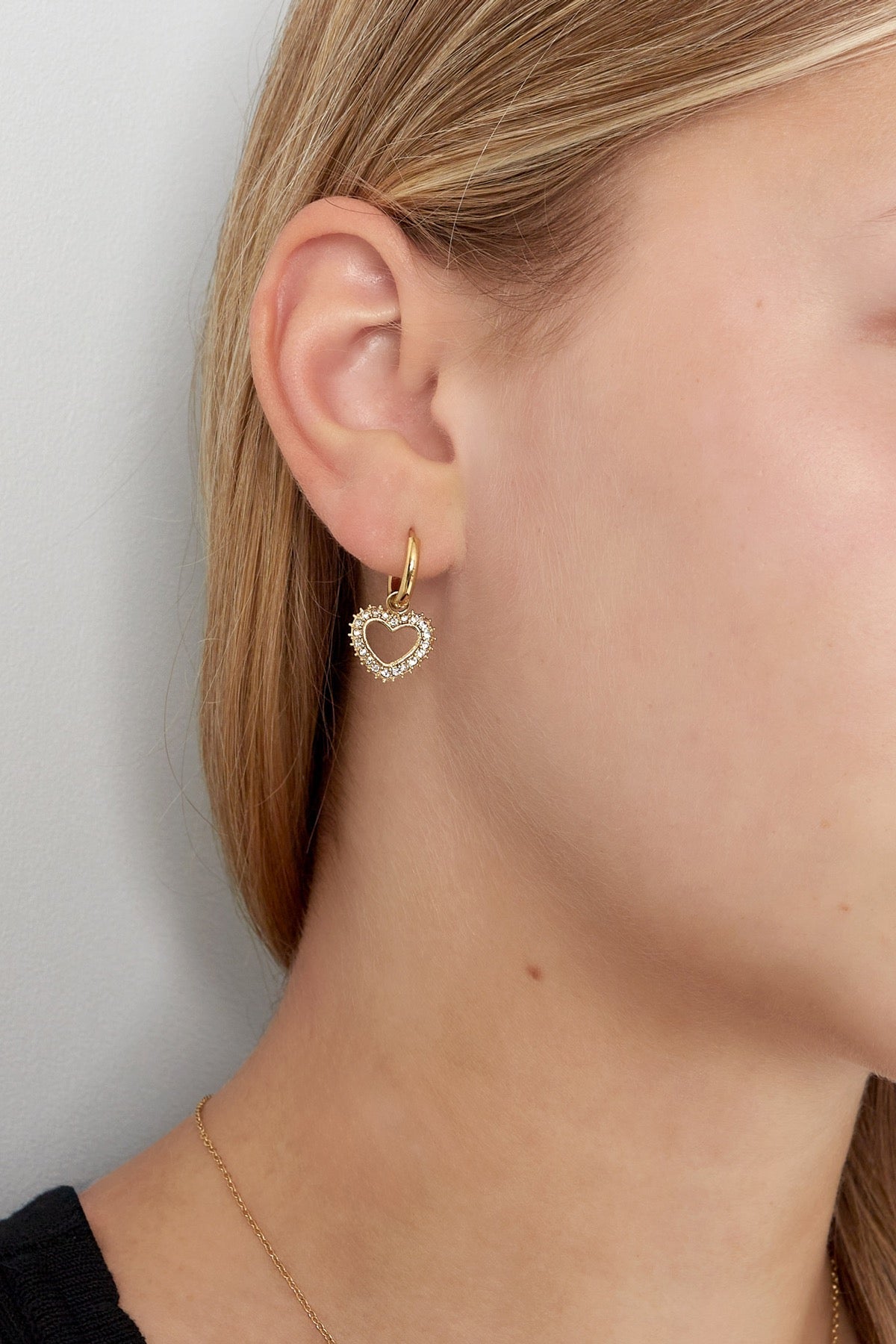 Detailfoto van een model met de gouden hartvormige oorbellen van Louxx the brand, die elegant zijn vastgelegd in een casual setting.