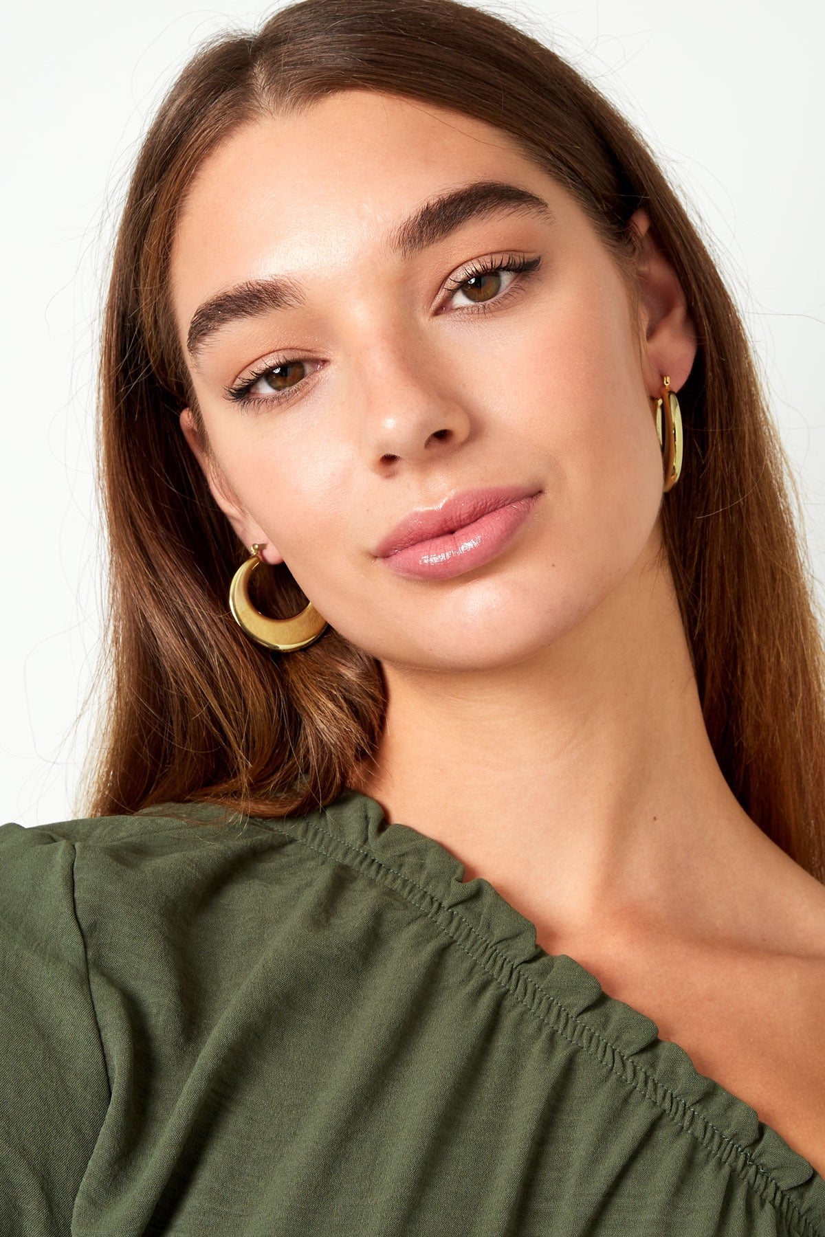 Une vrouw draagt elegante gouden Oorbellen | Rond van Louxx the brand, met een natuurlijke uitstraling en subtiele make-up.