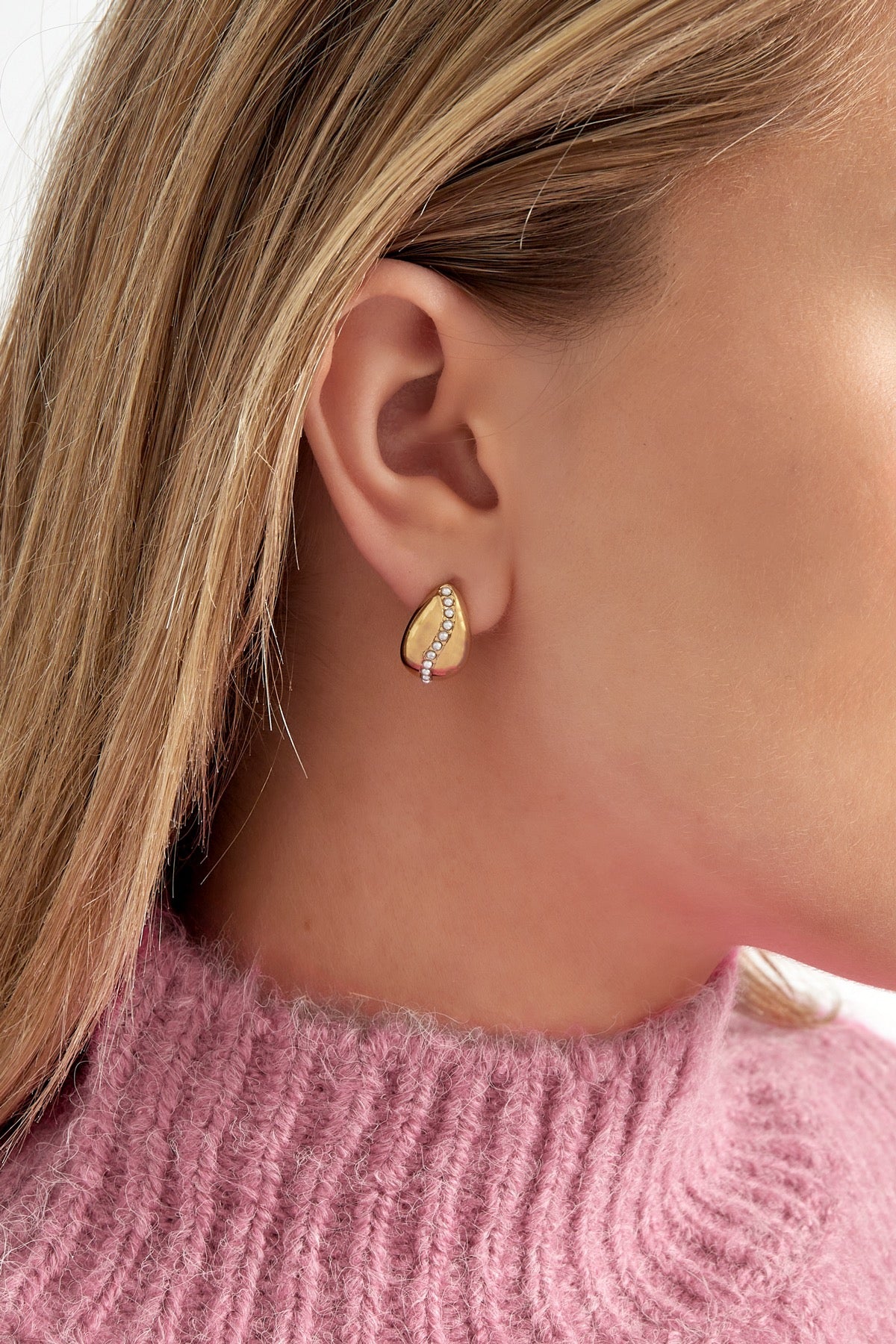 Model draagt de Oorbellen Sweet Pearl van Louxx the brand. De gouden oorbellen zijn zichtbaar in een casual setting met een roze gebreide trui.