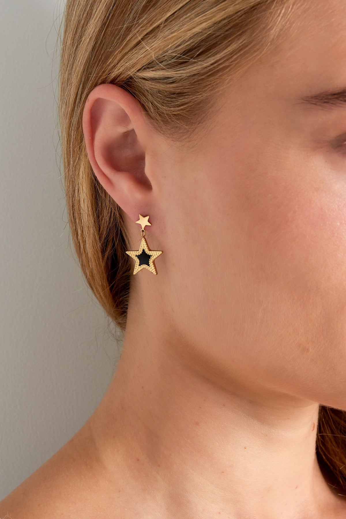 Close-up van gouden sterren oorbellen van Louxx the brand, gedragen door een model die de stijlvolle en unieke uitstraling benadrukt.