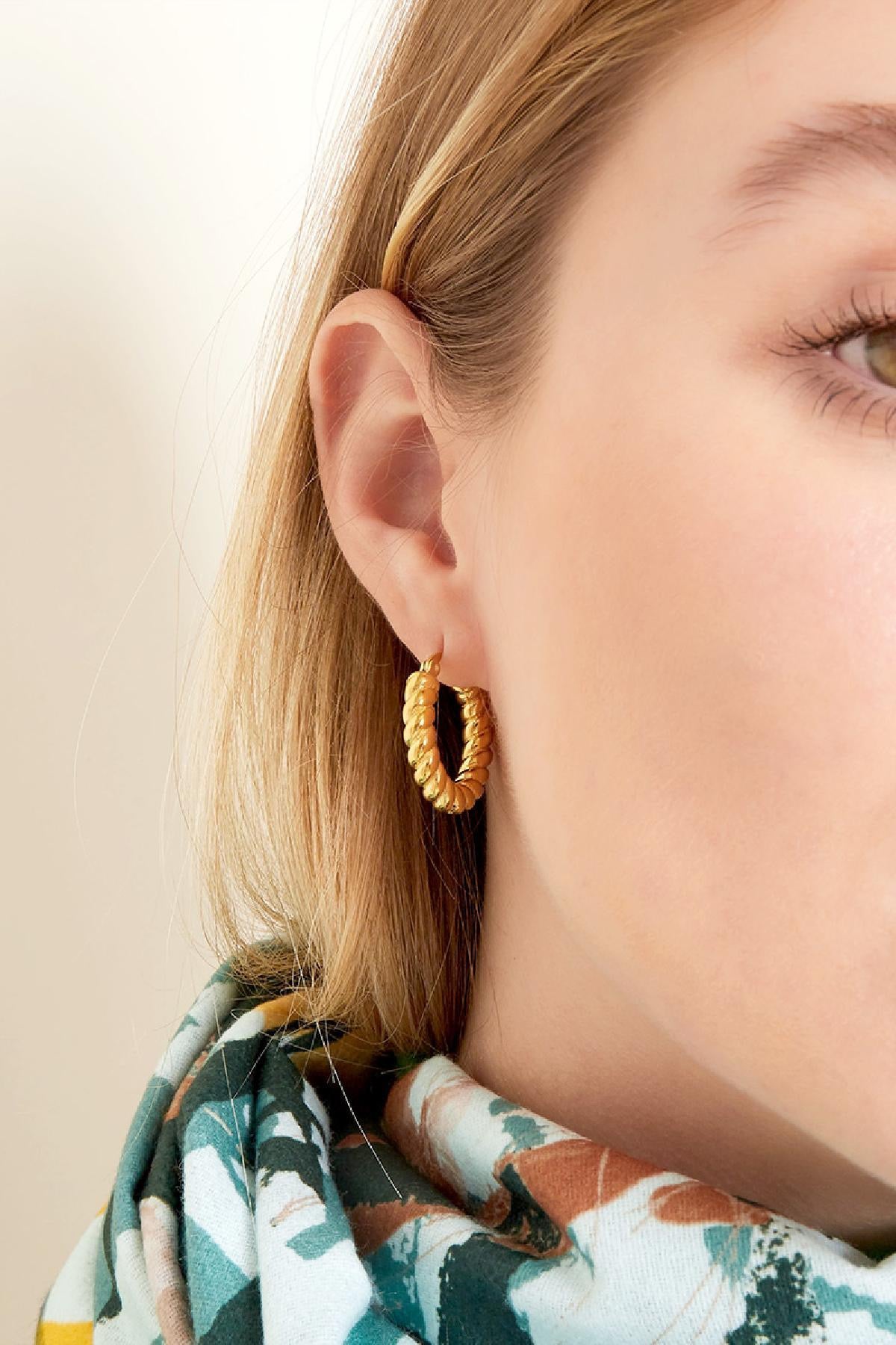 Vrouw met gedraaide gouden oorbellen van Louxx the brand, die elegantie en stijl uitstralen. Oorbellen | Gedraaid.
