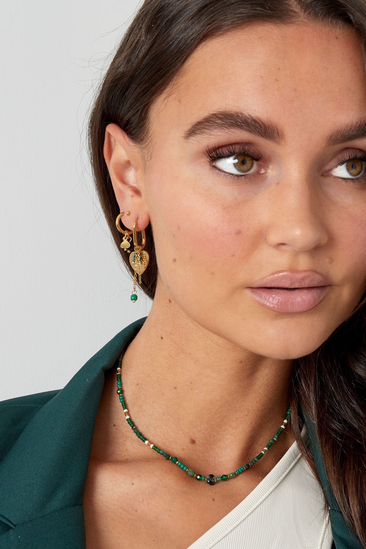 Dichtbij opname van het gezicht van een model met Oorbellen | Schoppen van Louxx the brand, gecombineerd met een elegante groene outfit.