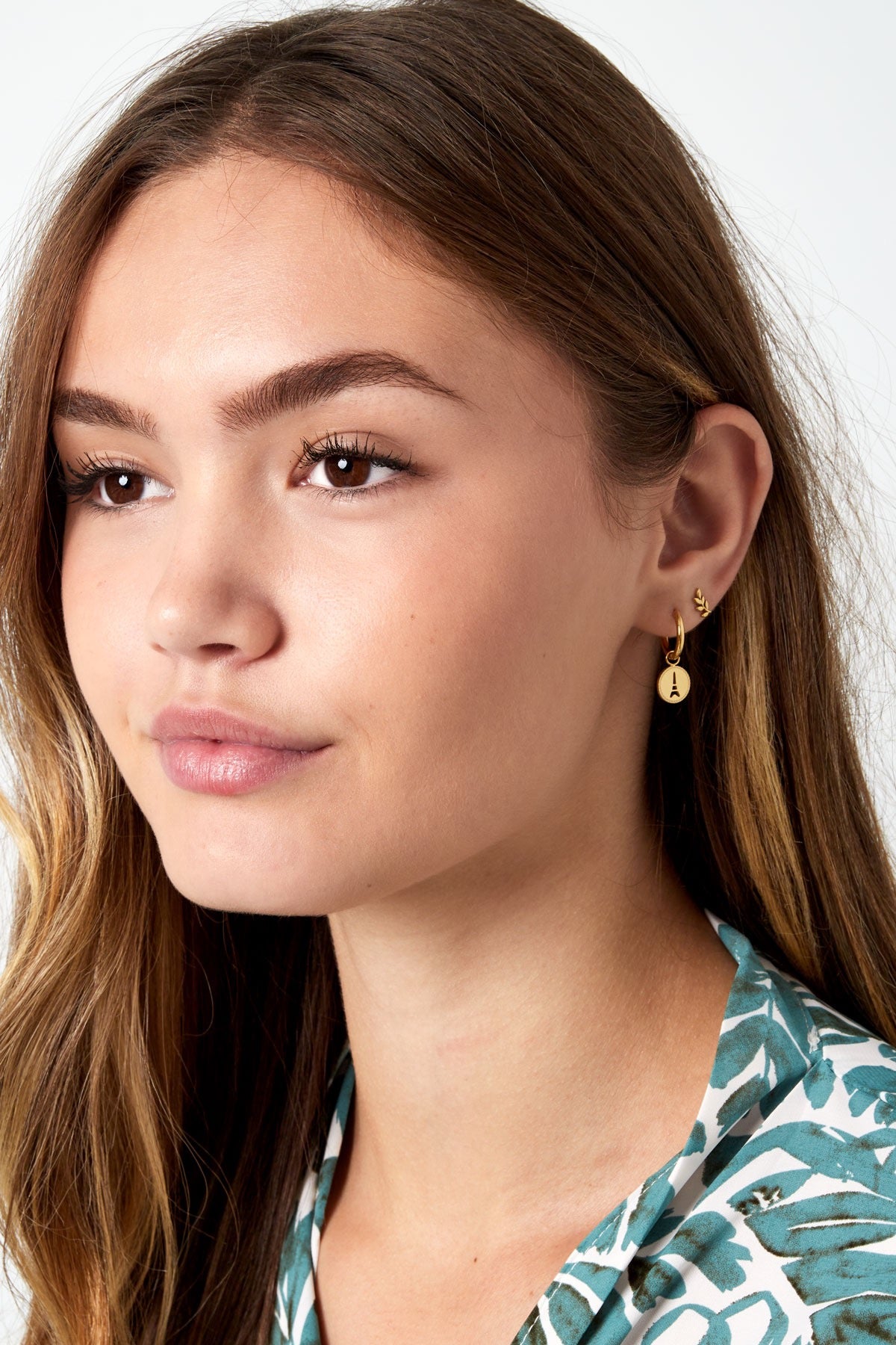 Een model poseert met gouden oorbellen van Louxx the brand, geĆÆnspireerd op Parijs, met de design titel 'Oorbellen | Parijs', die opvalt in het dagelijkse leven.