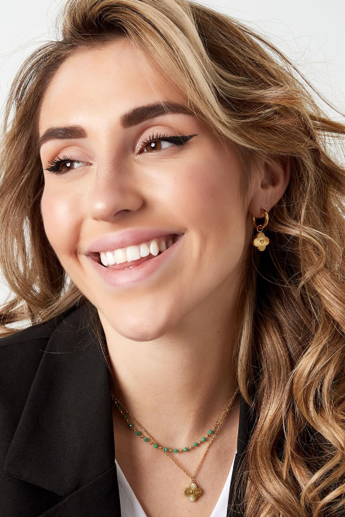 Vrolijke glimlach van een model met gouden Oorbellen | Bloem en een ketting, allebei van Louxx the brand. Geweldige aanvulling voor je sieradencollectie.