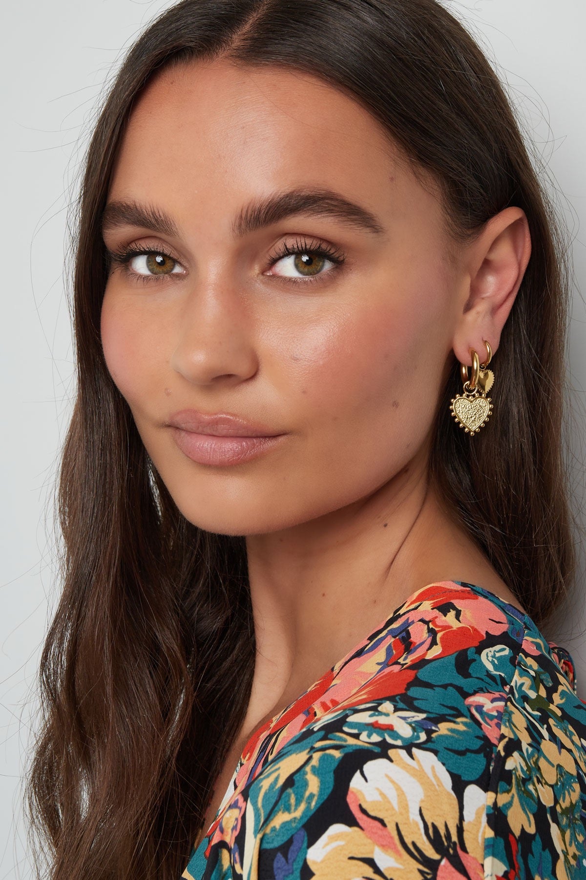 Stralend model met gouden hart oorbellen van Louxx the brand, glimlachend met een kleurrijke blouse die de oorbellen mooi accentueert.