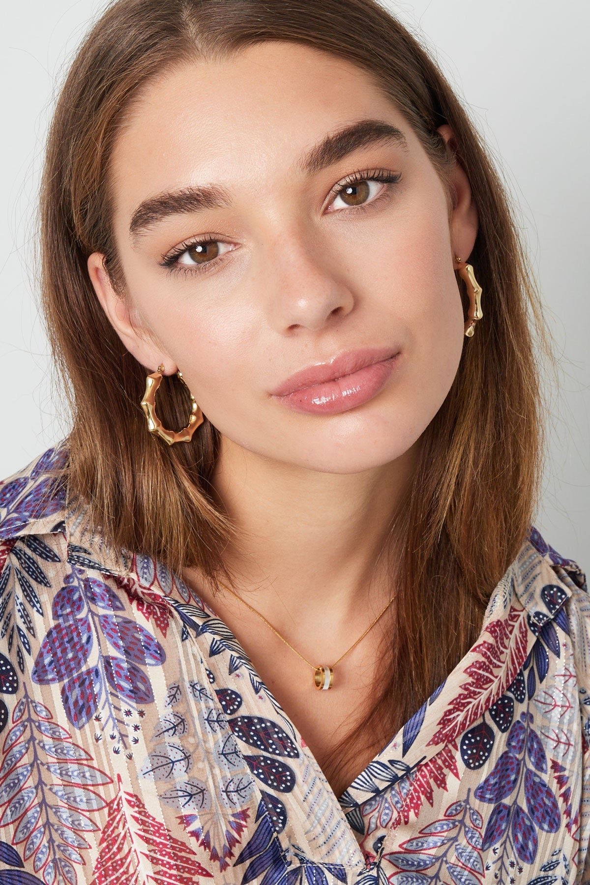 Close-up van een model dat Oorbellen | Kronkels in goud van Louxx the brand draagt, in een mooie outfit met een kleurrijke print.