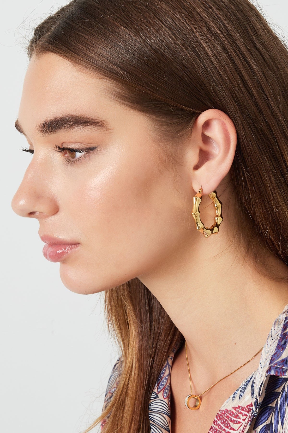 Model met Oorbellen | Kronkels in goud van Louxx the brand, die stijlvol zijn bevestigd aan haar oor.