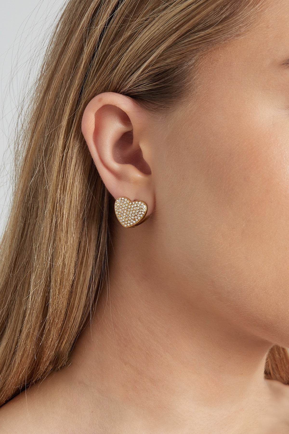Een model draagt de gouden hart oorbellen van Louxx the brand, perfect voor een trendy look.