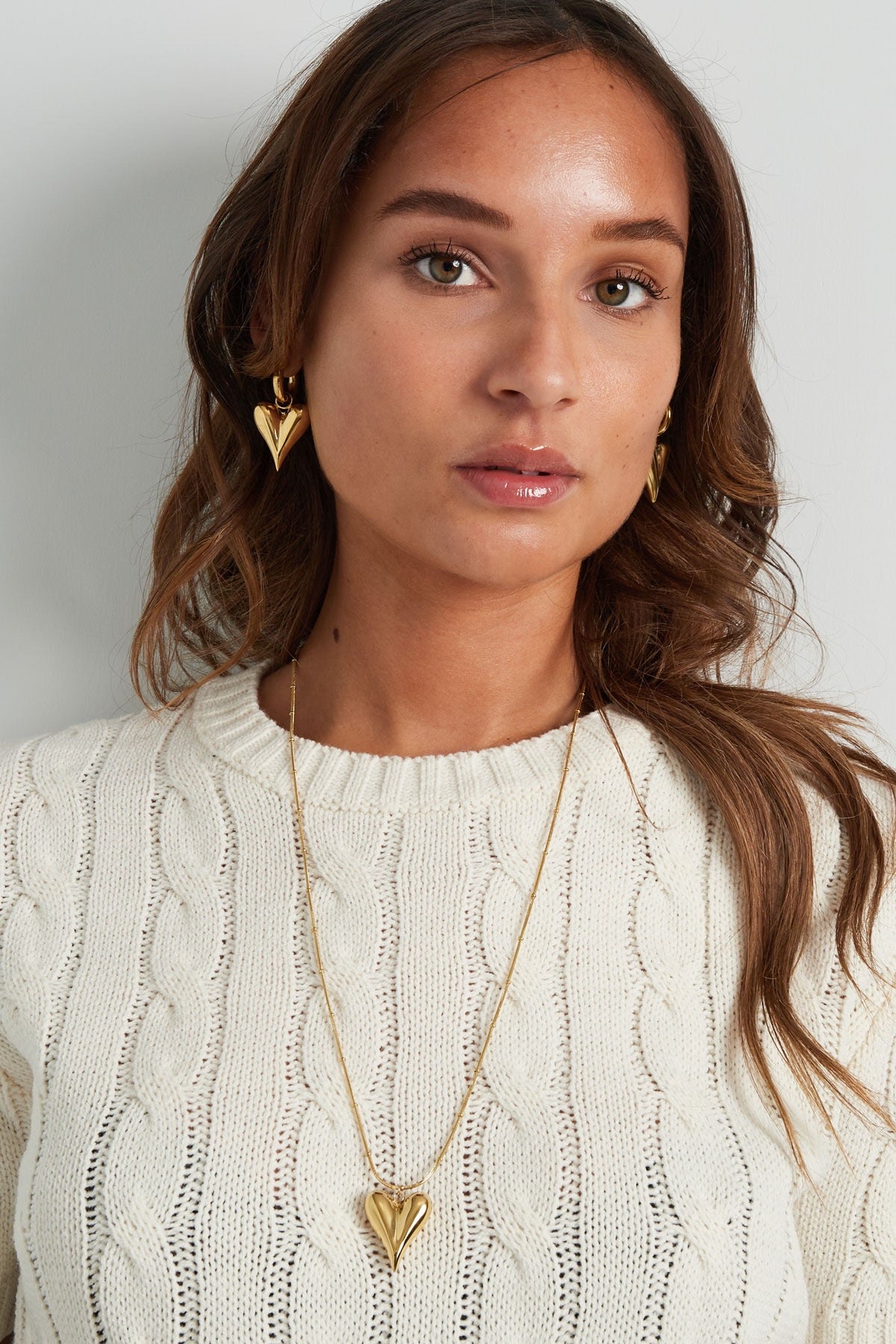 Model poseert met gouden hart oorbellen van Louxx the brand en een bijpassende halsketting, perfect voor een trendy look.