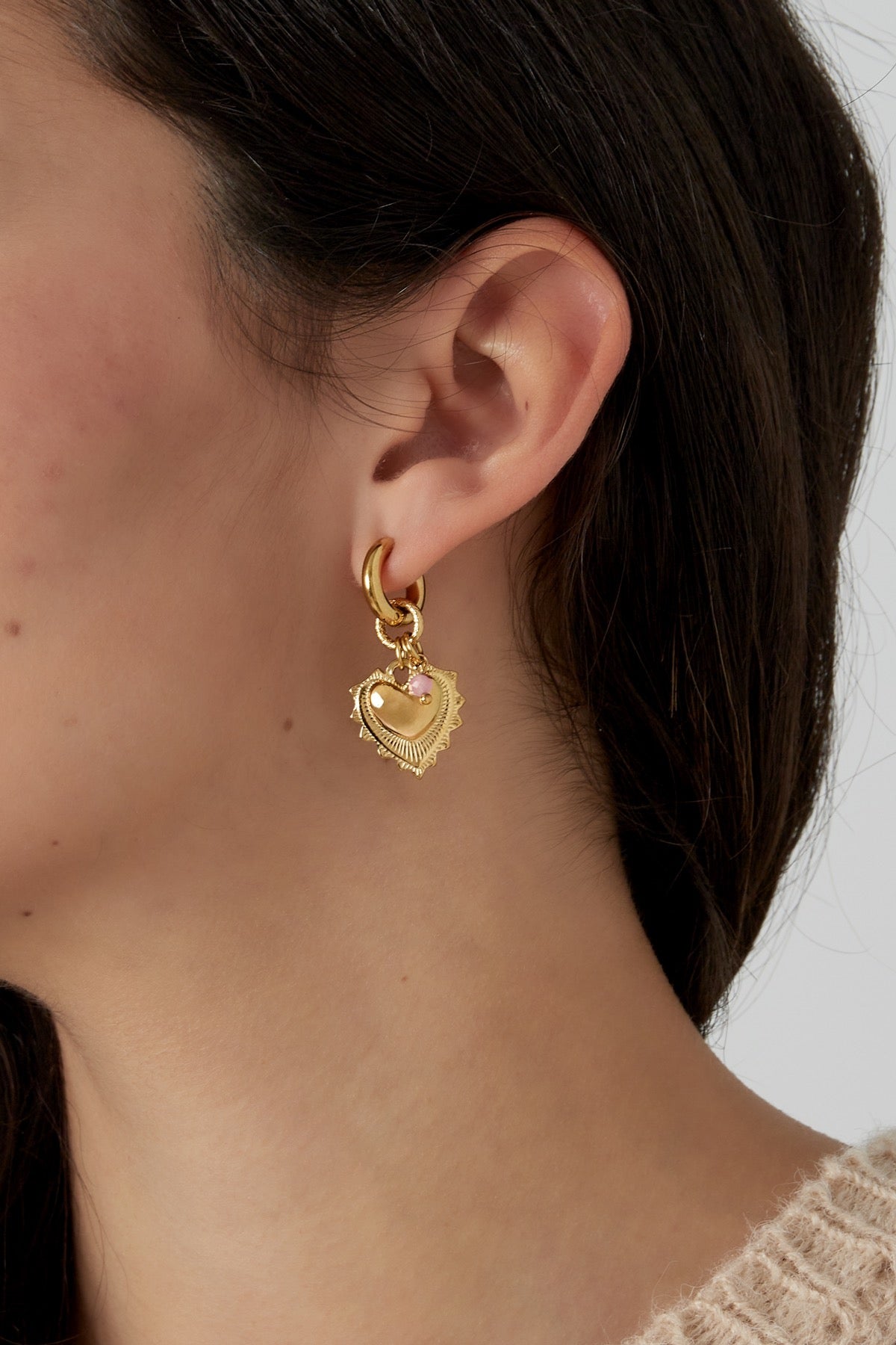 Model die Oorbellen | Hart van Louxx the brand draagt, close-up van de gouden hartvormige oorbellen met een roze accent.