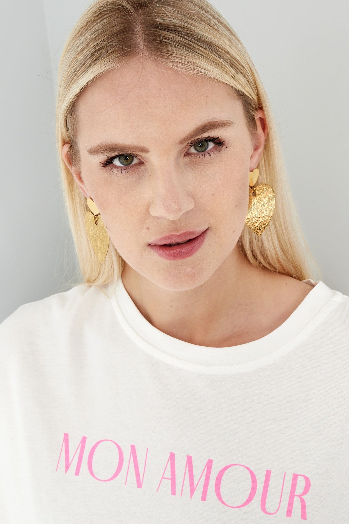 Model in een casual outfit met gouden hart oorbellen van Louxx the brand. Geweldig voor een moderne look.