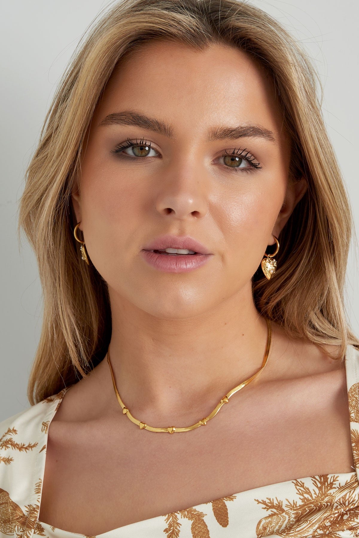 Een model draagt gouden hart oorbellen van Louxx the brand, met een casual look en een gouden halsketting.