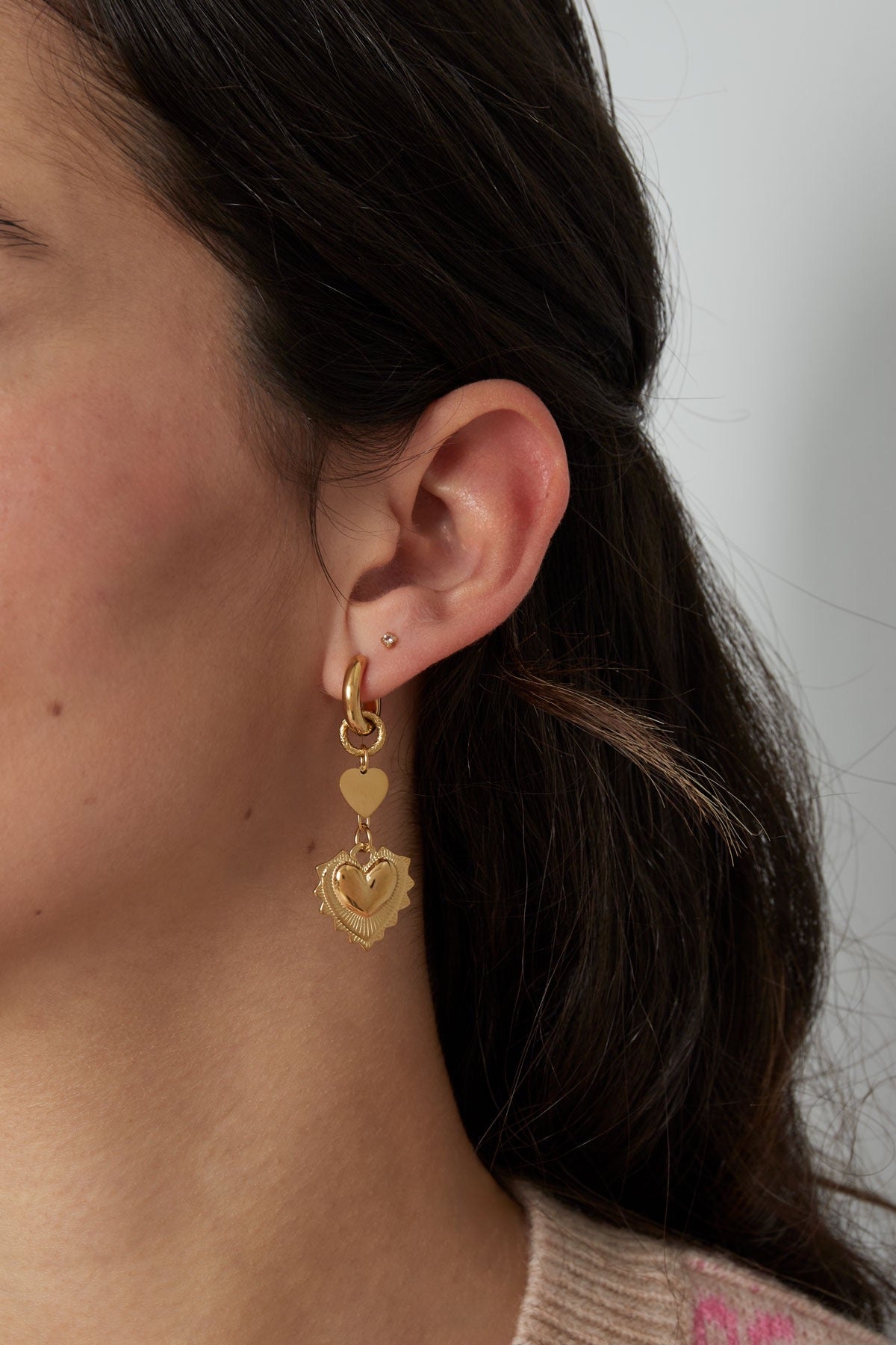 Model draagt gouden hart oorbellen van Louxx the brand. De oorbellen zijn elegent en veelzijdig, ideaal voor een casual look.