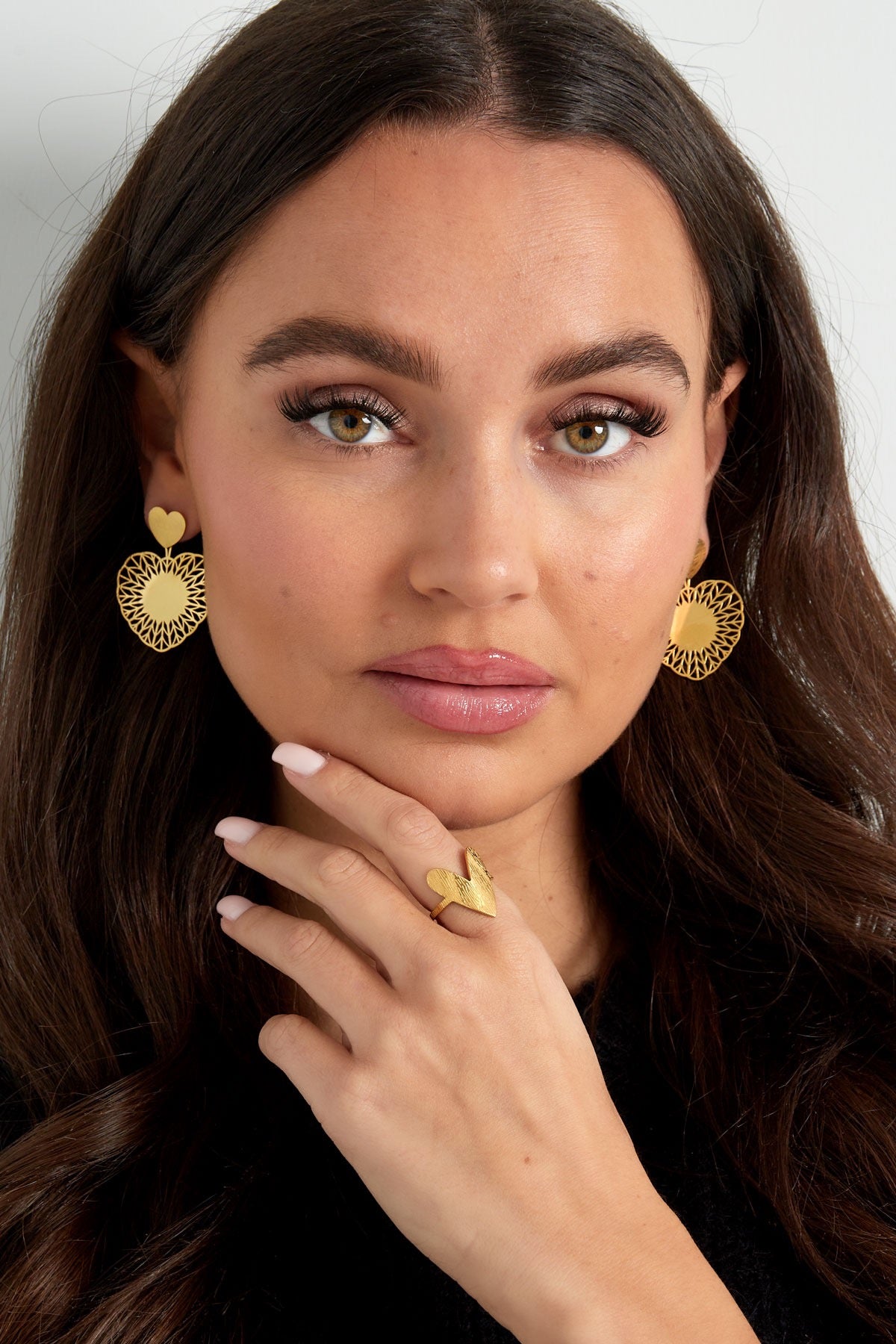 Model poseert met gouden hart oorbellen van Louxx the brand en een bijpassende ring, een fashionable combinatie.