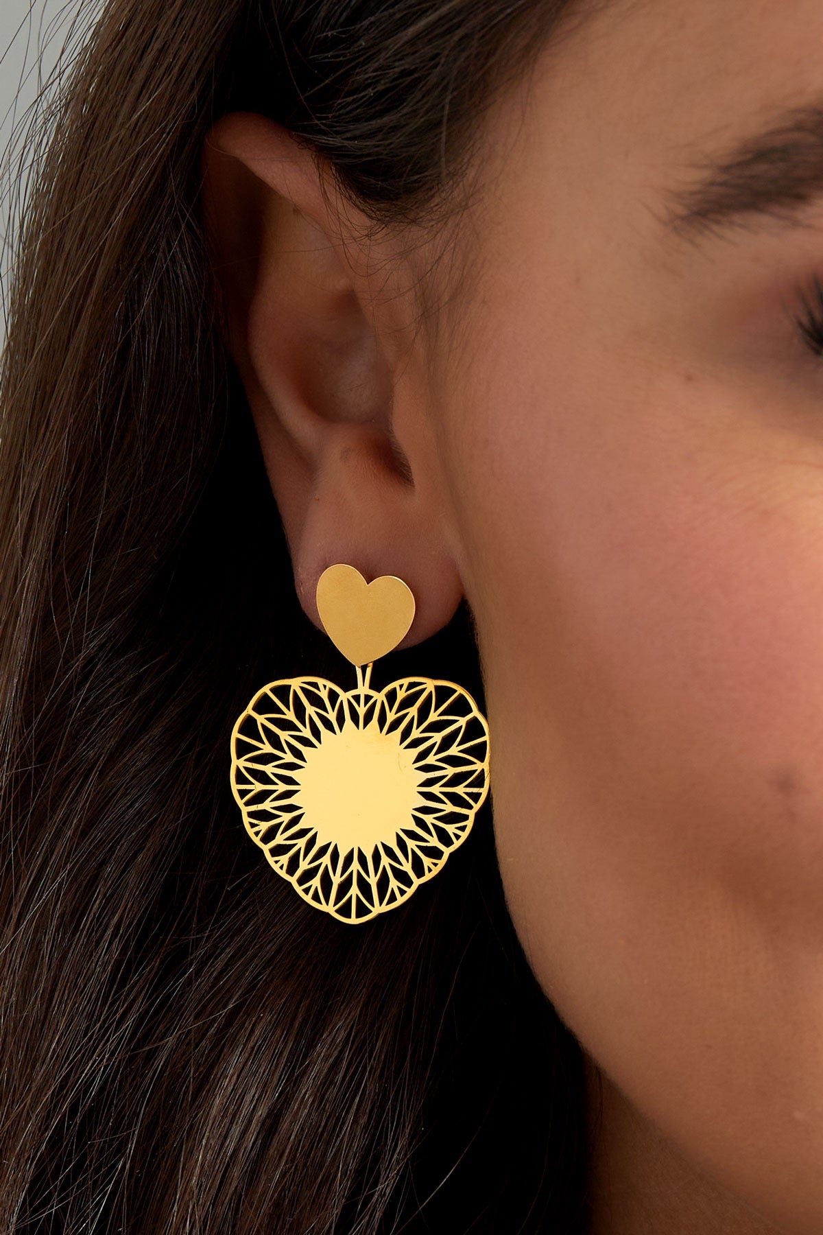 Een model draagt de gouden hart oorbellen van Louxx the brand, perfect voor een casual look.
