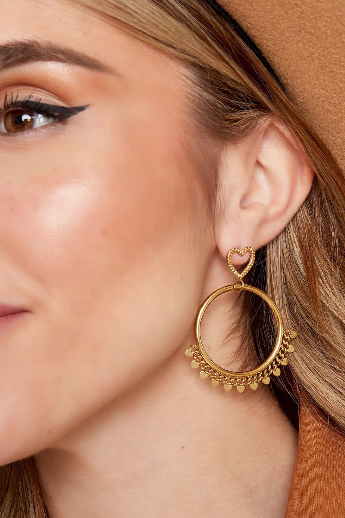 Close-up van een vrouwelijk gezicht met gouden hart oorbellen van Louxx the brand. De oorbellen zijn extra zichtbaar naast het hoofd met een natuurlijke uitstraling.