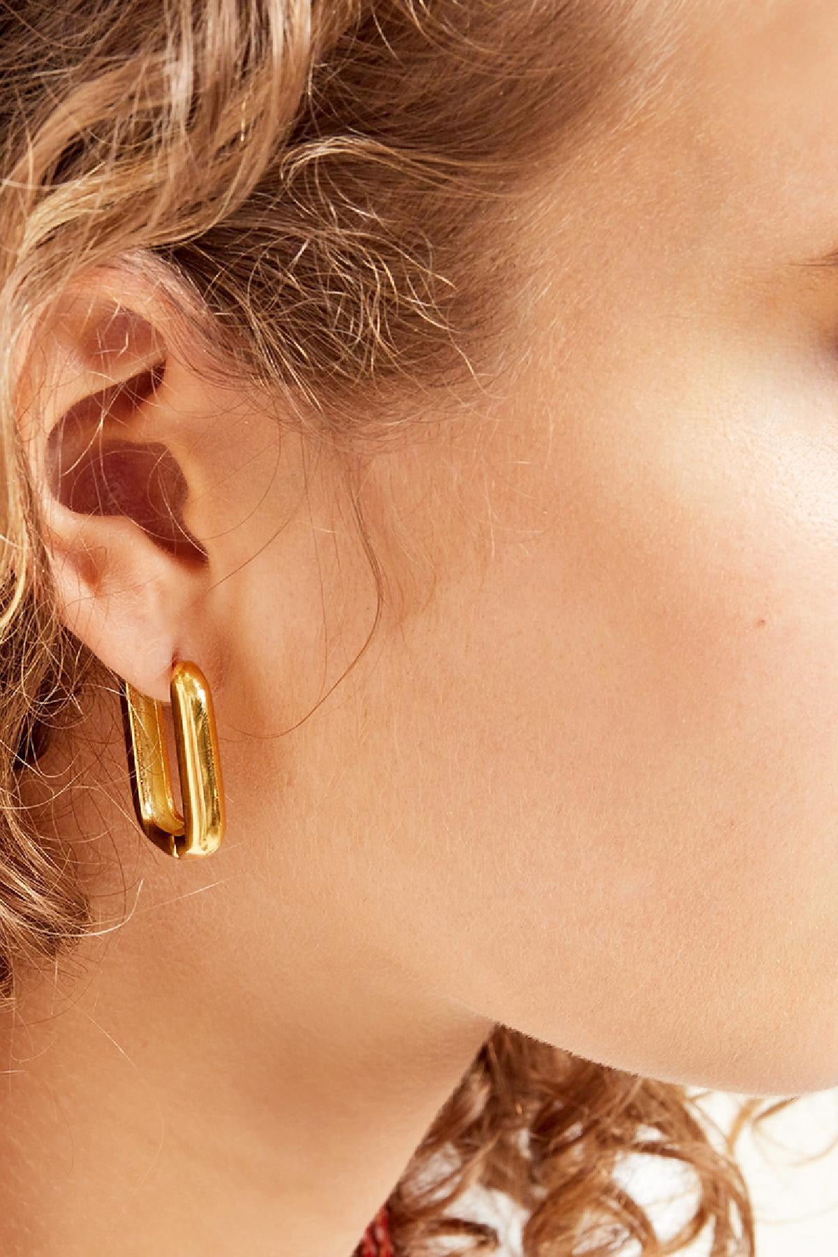 Oorbellen | Vierkant van Louxx the brand. Close-up van gouden vierkante oorbellen die elegant tegen de huid van de model stralen.