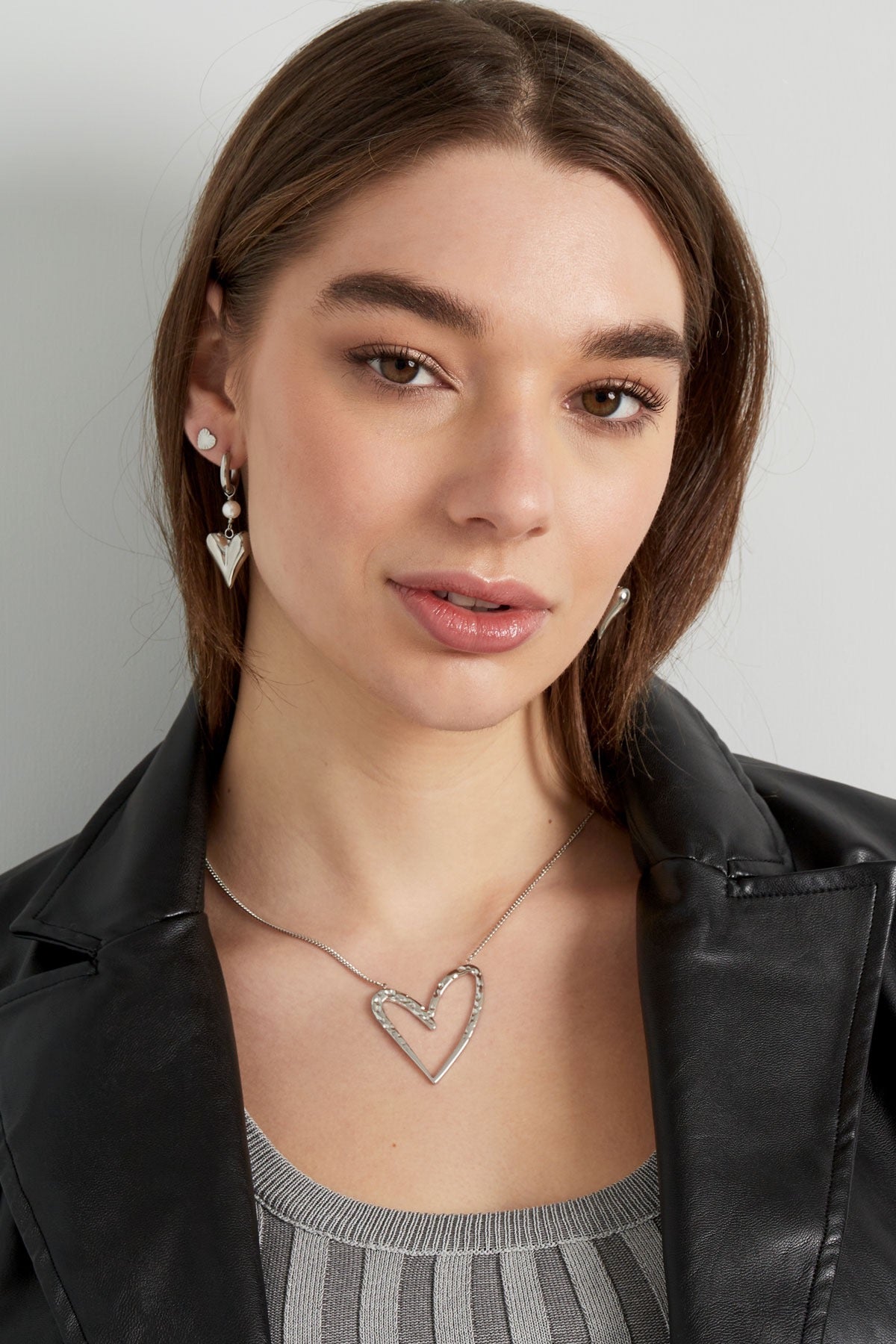 Close-up van een model met Oorbellen | Hart en bijpassende ketting van Louxx the brand. De zilveren accessoires stralen stijl en flair uit.