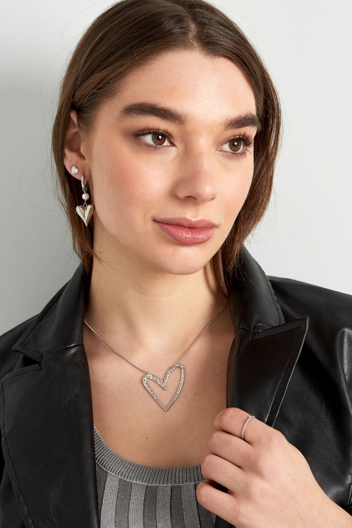Model die de Oorbellen | Hart van Louxx the brand draagt. Deze oorbellen zijn zilver en hebben een hartvormige hanger, gecombineerd met een elegante ketting.