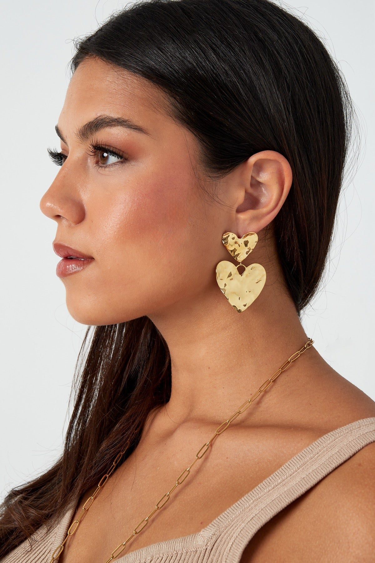 Zijaanzicht van een vrouw met gouden hartoorbellen en een minimalistische ketting, perfect voor een chique en elegante look