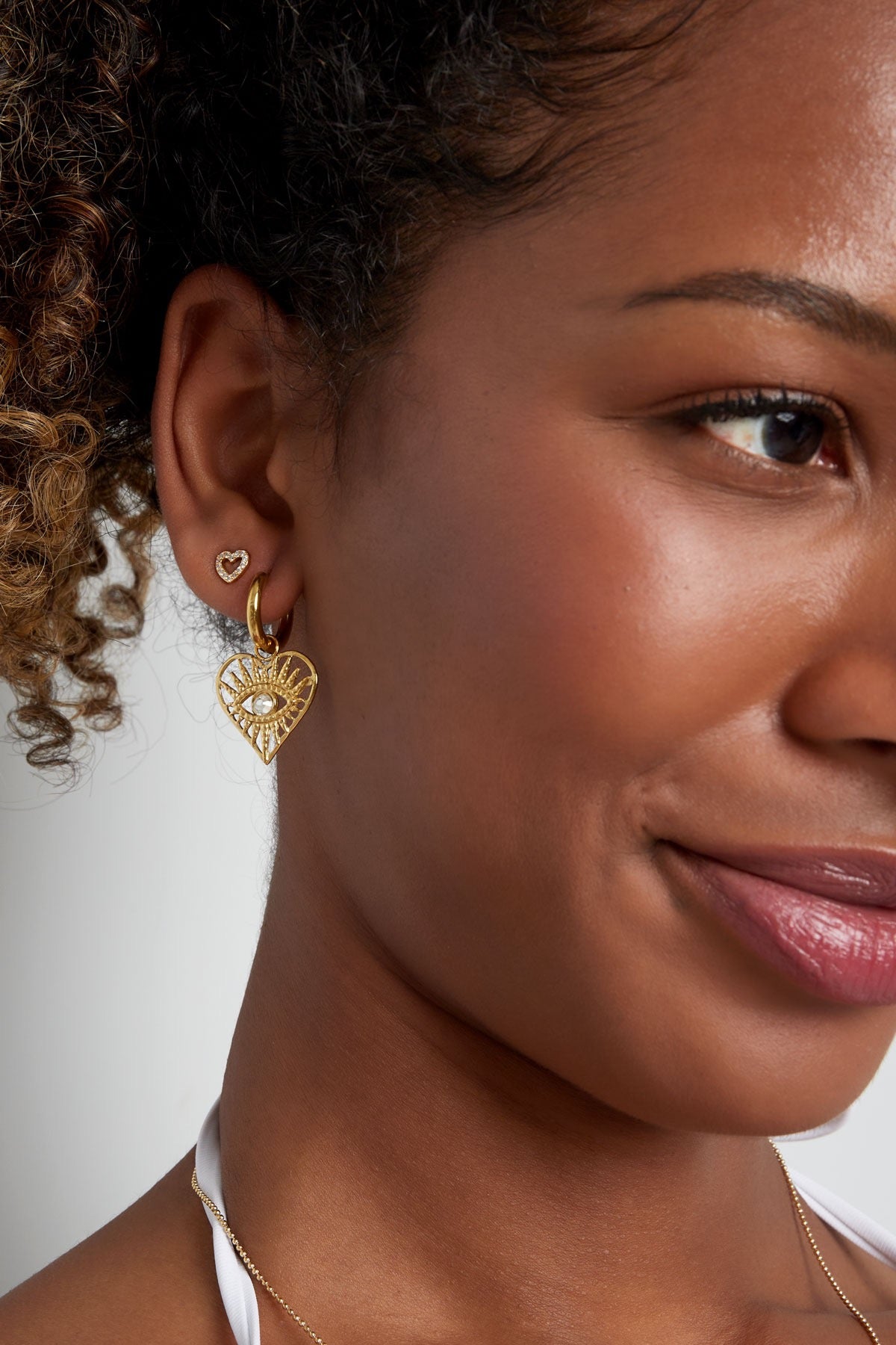 Gouden hartvormige oorringen met een verfijnd opengewerkt design en een oogdetail in het midden, perfect voor een elegante en trendy look.